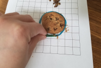 Chocolate chip cookie on grid paper, pile of chocolate chips beside it. Paperclip moving cookie fragments back into the original cookie outline.