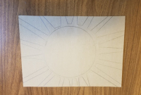 A piece of cardboard on a tabletop with a sun sketched on it in pencil.