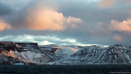 A late summer vista in the Canadian Arctic showing ocean and snow-peaked mountains.