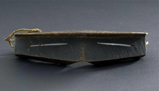 Inuit snow goggles resembling a dark wooden rectangle with a downward protrusion toward the nose, and two slits to see through.