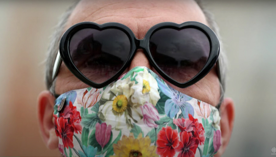Woman wearing heart-shaped sunglasses and floral face mask.