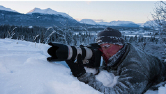 Man laying in the snow taking a photograph.