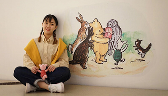 Girl sitting beside Winnie illustration holding a Piglet doll.