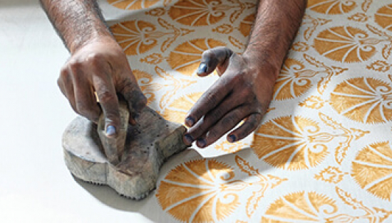 Hands pressing a stamp with yellow paint onto white fabric.