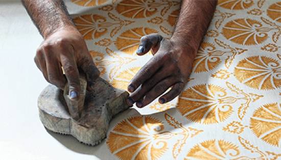 An Indian textile worker uses a wood stamp to print an orange-yellow flower pattern on white cotton. 