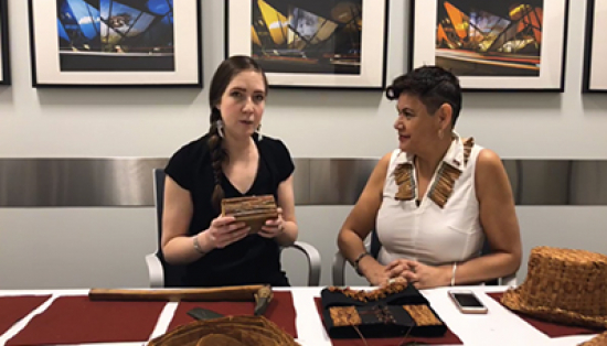 ROM staff Jessie Jakumeit and J’net Ayayqwayaksheelth hold a cedar block and sit at a table displaying four objects made using cedar bark.