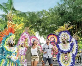Two people dancing with touristy like clothes while surrounded by people are in bright feathers, dancing.
