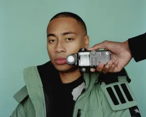 A man posing for the camera with a recorder being held in front of him.