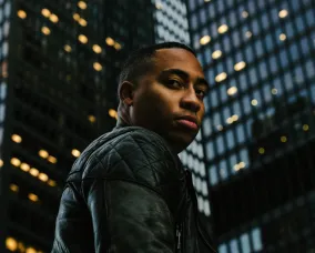 Cadence weapon looking over his shoulder with two high rise buildings in the background.