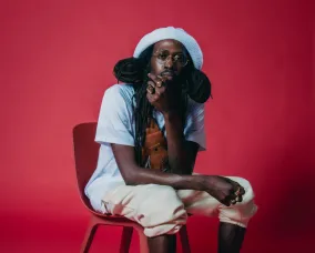Junia T. sitting on a chair with white clothing and a red background.