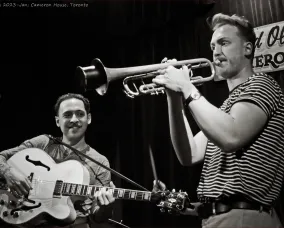 Two men playing music on a guitar and trumpet in black and white.