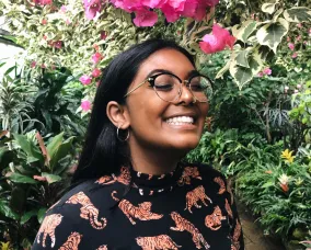 A grinning South Asian person with long dark hair wearing a black top with tigers on it.