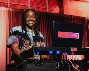 DJ HustleGRL smiling behind her DJ equipment.
