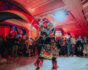 An Indigenous man in regailia dances with hoops in front of a crowd