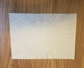 A piece of cardboard on a tabletop with a sun sketched on it in pencil.