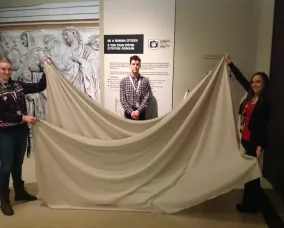 Deux jeunes femmes brandissent un long morceau de tissu blanc devant un jeune homme.