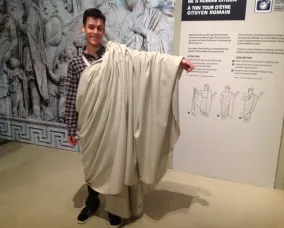 Le jeune homme se tient debout, la toge enroulée sur son épaule gauche.