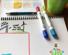 Version colorée de la conception d'une école durable. Plusieurs marqueurs sont posés sur le papier.