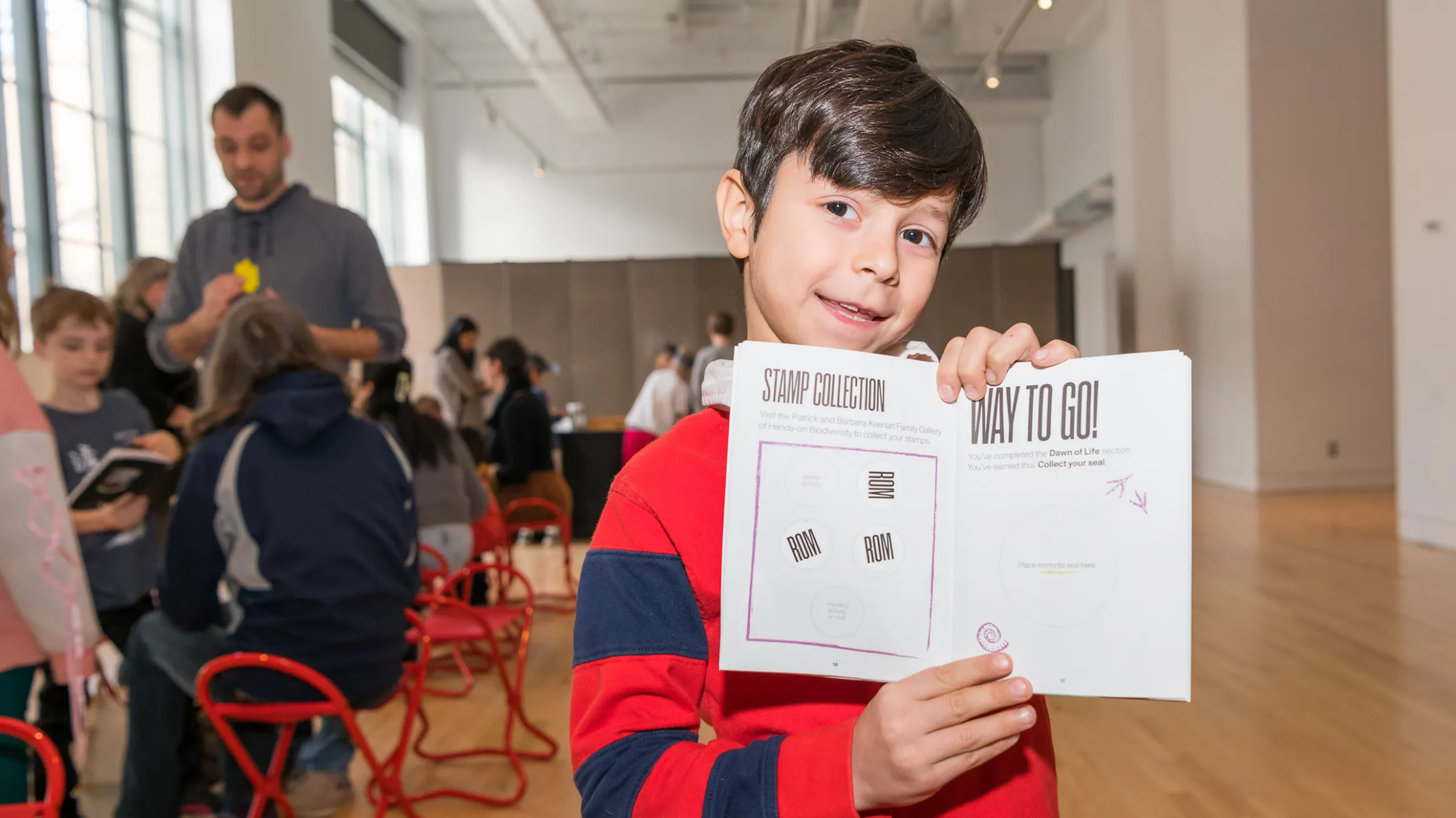 A boy excitedly holds an open activity book showing his stamps and stickers.