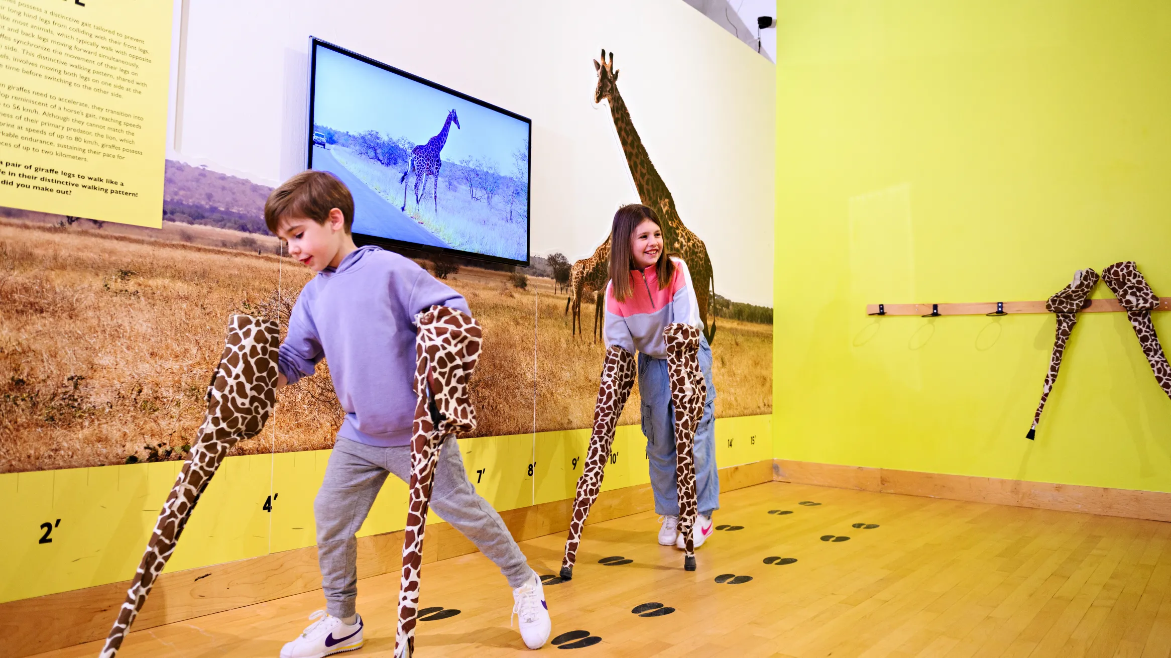 2 children at THEMUSEUM with their hands in giraffe legs
