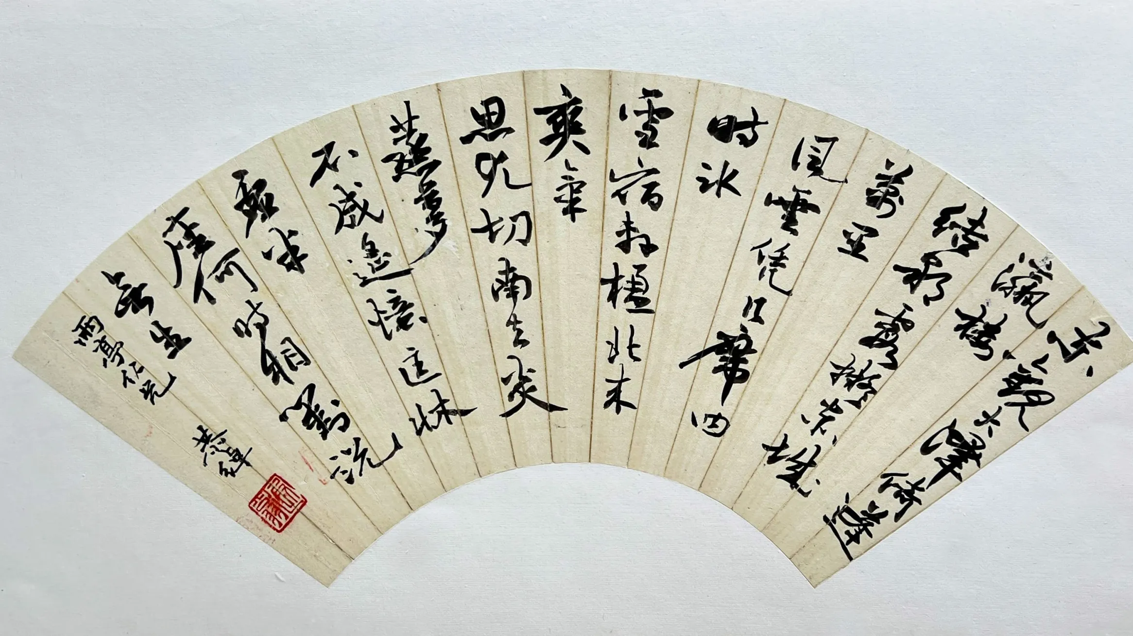 Fan-shaped artwork featuring traditional Chinese calligraphy in bold black ink on a cream background, with a red seal stamp