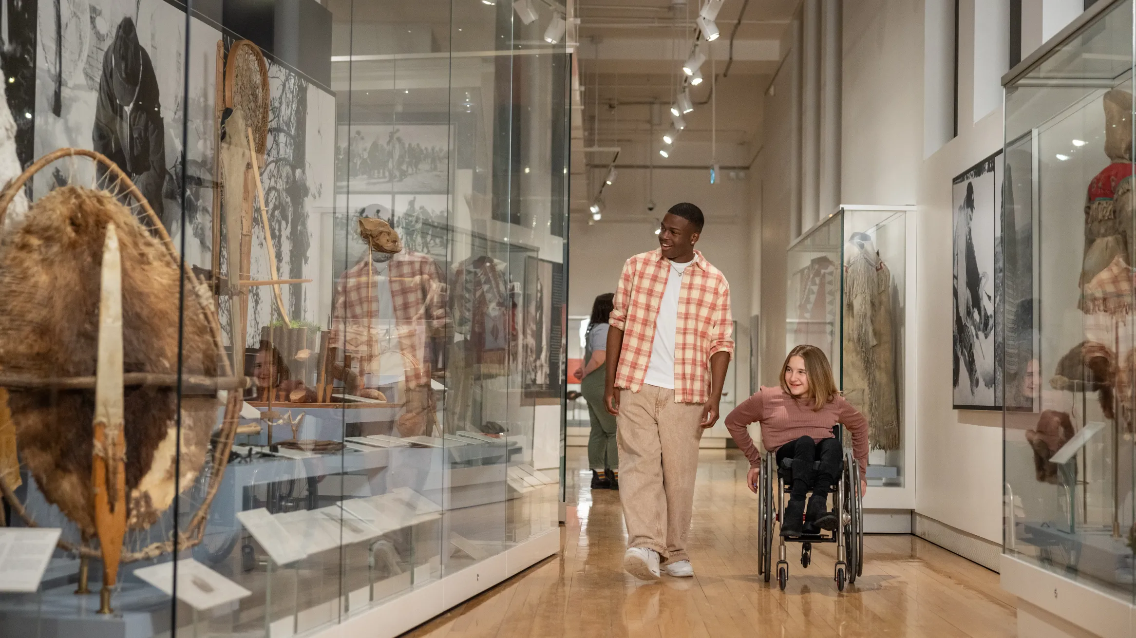 A guy in a plaid shirt walking with a girl in a wheelchair looking at museum collections at ROM