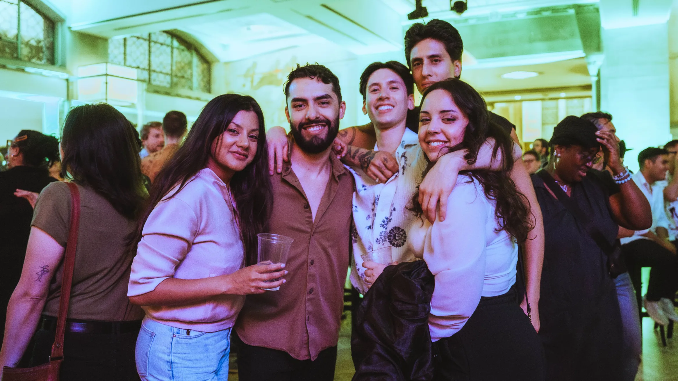 A group of people posing in a crowd with a green lighting in the background.