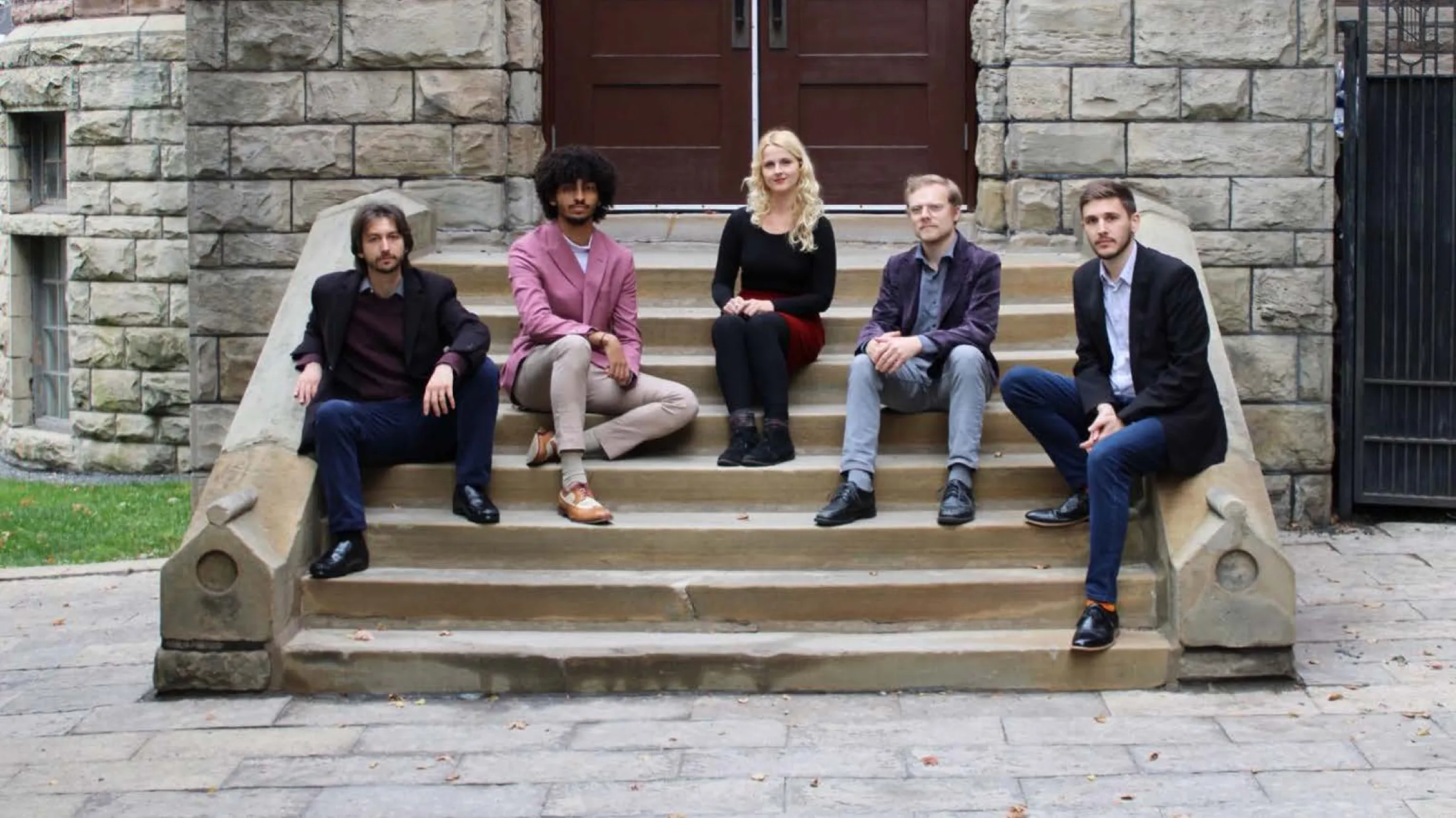 Diapente Renaissance Vocal Quintet Five young people sit facing the camera on the stone steps of a historic building.