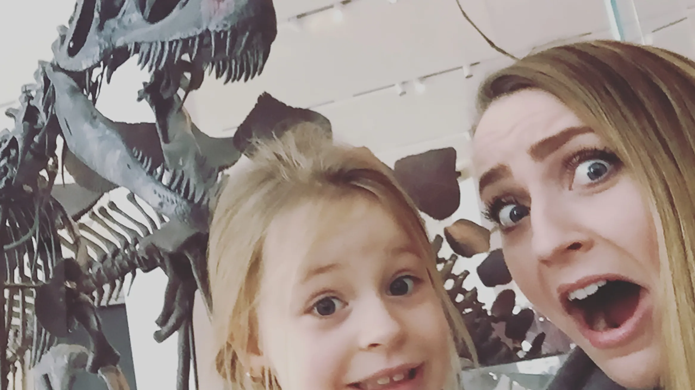 A young woman and a child pretend to be scared in front of a T.rex skeleton