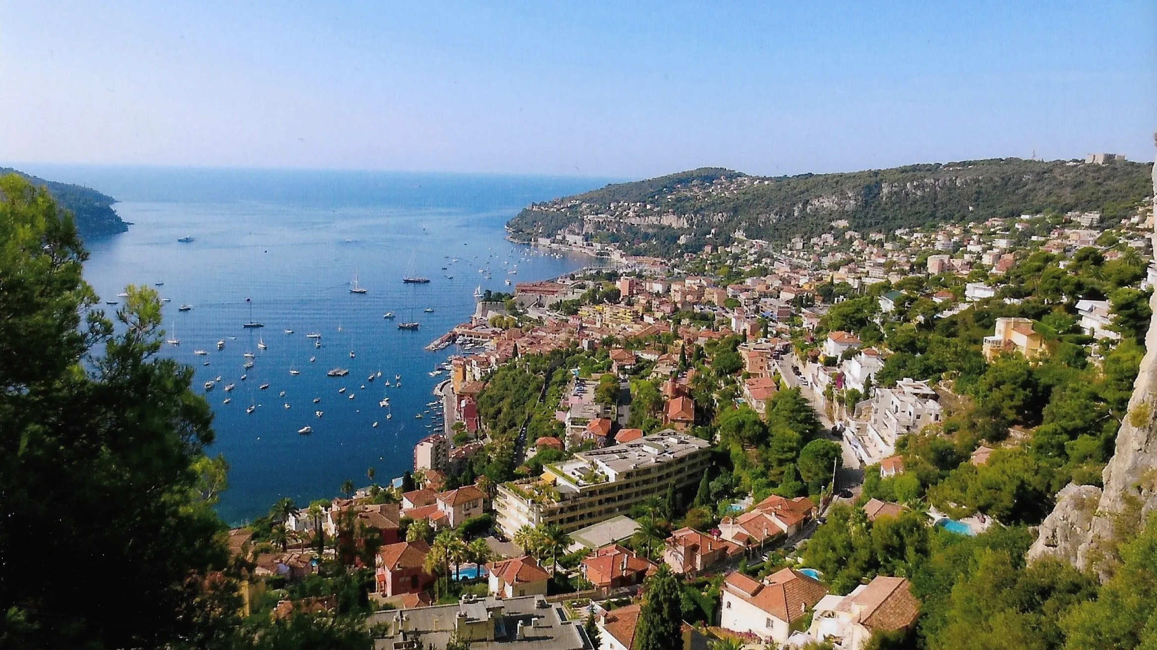 A picturesque coastal town with numerous buildings, and a beautiful, calm sea with several boats.