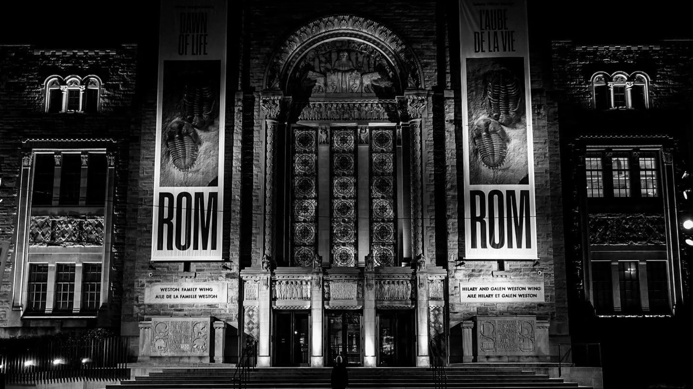 Black-and-white view of the ROM’s ornate entrance illuminated at night.