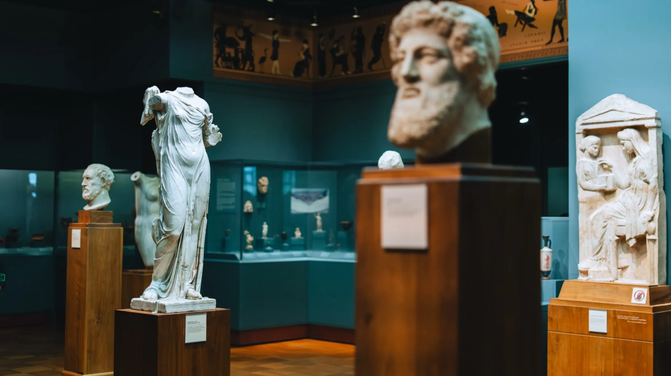 Ancient Greek statues and marble reliefs displayed in a museum gallery.