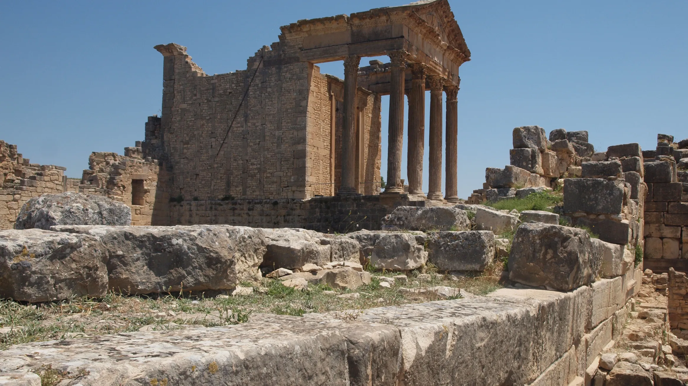 The ruins of an ancient temple with weathered columns and a clear blue sky in the background